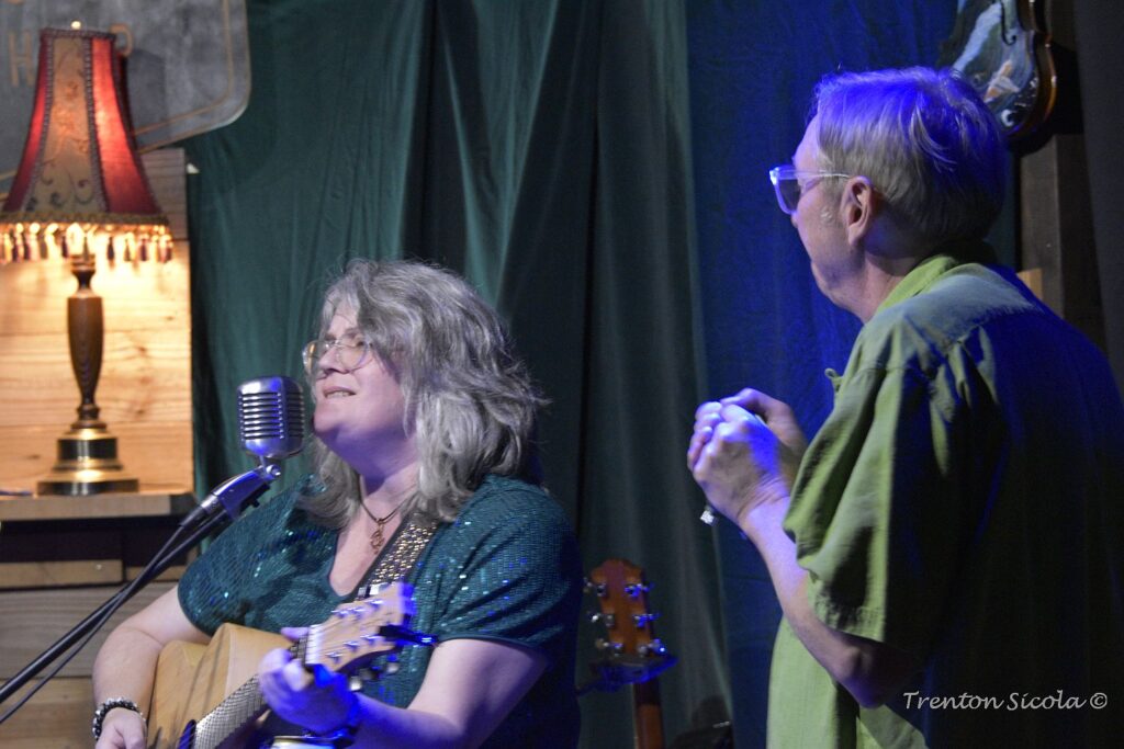 Patty singing and playing guitar while Conner looks on with harmonica