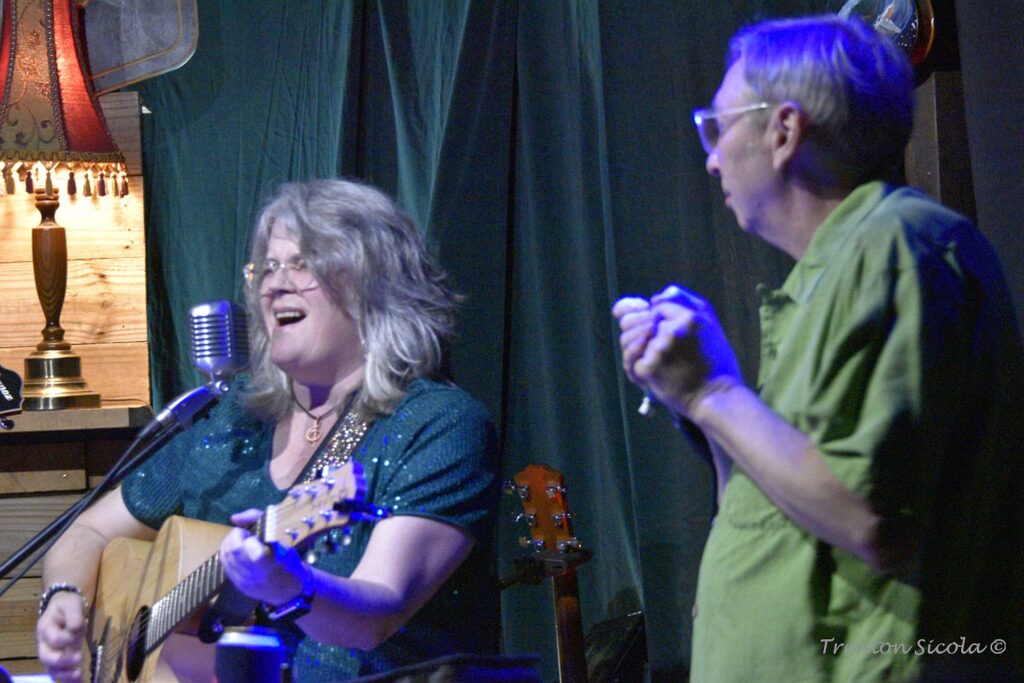 Patty singing and playing guitar while Conner looks on with harmonica