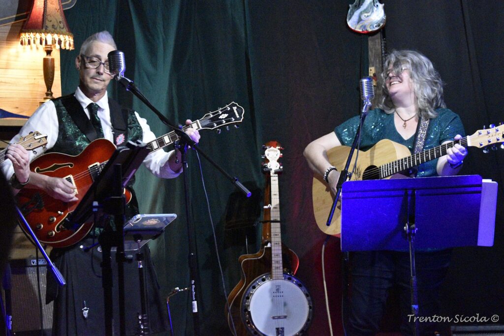 Matt Donald and Patty Richmond smile on stage with guitars